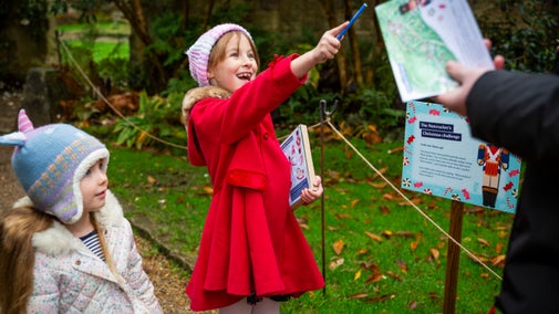 Two children, one in a bright red coat, excitedly pointing out a trail point.